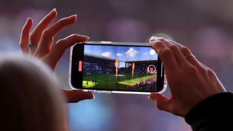 A mobile phone is held up to record a video at a Premier League match