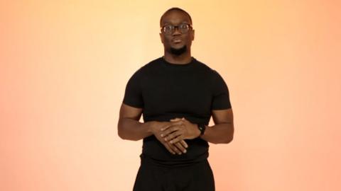 Sage Todz in glasses and a black T-shirt in front of a pale orange background