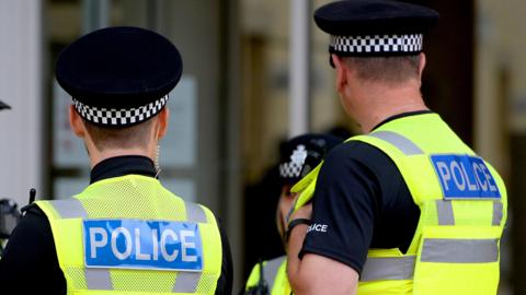 The back of two police officers wearing fluorescent stab vests