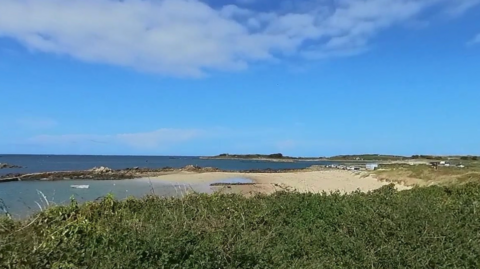 Amarreurs beach in Guernsey, showing the white sand and blue sea, amidst a cloud-free sky. 