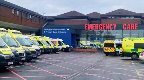 A number of ambulances outside an A&E - a sign reads: EMERGENCY CARE