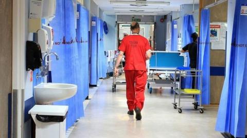 Man in red scrubs walking down a hospital ward