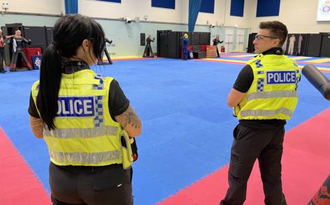 The back of two Wiltshire Police Officers wearing uniform in the training hall at police headquarters in Devizes