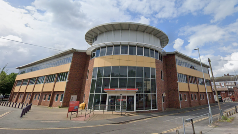 The front entrance to Swann House in Stoke-on-Trent - a four-storey building divided into three sections. The middle section, where the entrance is, is of a circular shape. 