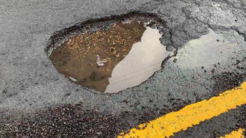A pot hole on a road is filled with water and next to a double yellow line