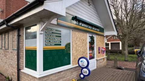 The storefront of St Pancras Stores in Lewes has its windows boarded following a previous attack. A Christmas wreath hangs from the upper entry door frame.