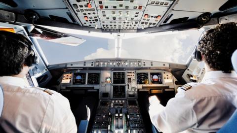 Two pilots sitting in a cockpit at plane controls.