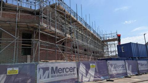 Building site showing three storey brick structure surrounded by scaffolding