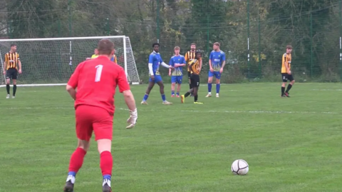 A scene from Saturday's match with a goalkeeper in a red kit and with 1 on his back readying himself to take a free kick from inside his own half.