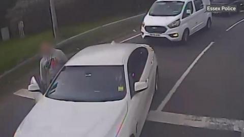 A BMW driver stood next to his white vehicle, with other vehicles queued up behind