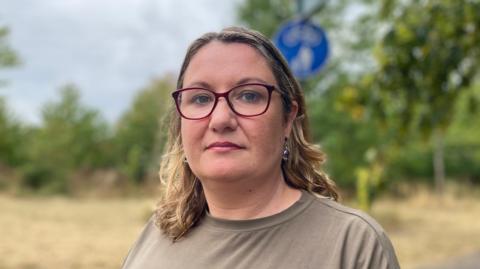 Woman, with glasses and wearing a khaki top, standing in a field.