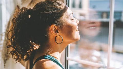 A woman looking out of a window with light shining on her face