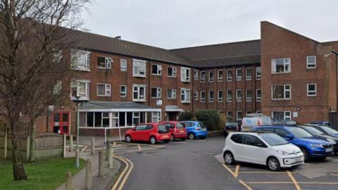 Rydal Court in Morecambe, a red brick three storey block of flats with white windows and cars parked outside the front in a car park