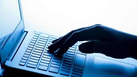A picture of a hand typing on a laptop keyboard. It is a light laptop with a shadow of a hand.