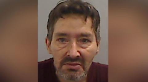 Mugshot of Robson. he has a haggard looking face, with a short dark beard and messy dark hair.