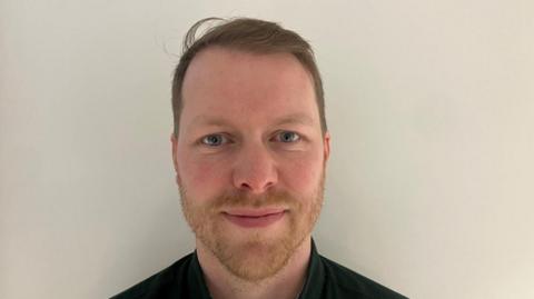 Javed Love is looking directly at the camera. He has a ginger beard and short light brown hair.