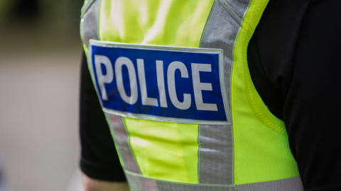 A generic image of the back of a police officer's jacket. The word police is in white on a blue background. 