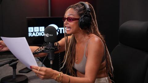 Alesha Dixon holding up a piece of paper and singing into a microphone