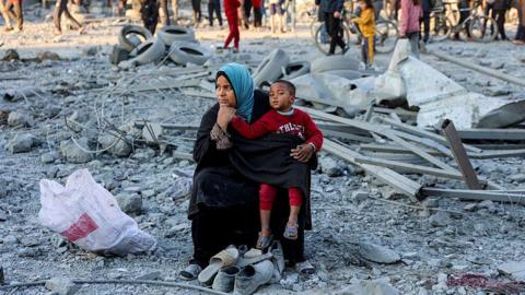 A woman child sit among grey rubble, pensively. 
