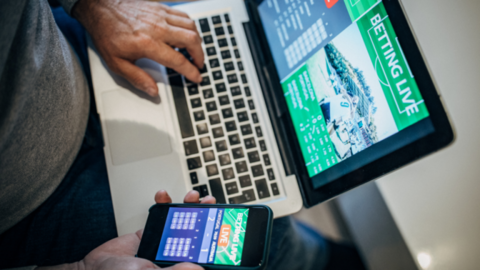 Man accessing gambling platforms online via laptop and phone app.