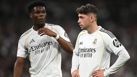 Real Madrid's Aurelien Tchouameni and Federico Valverde stand next to each other in a match, wearing the club's white kit