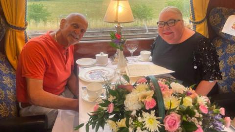 Claire and Rob sit on an exclusive looking train with flowers