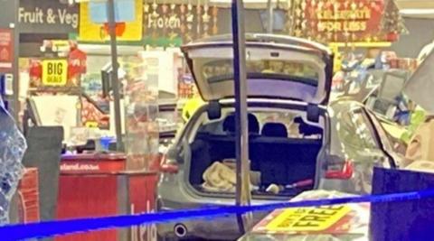 A car with the boot up inside an Icelend store. Signs are at the top of the image, including Fruit & Veg and Frozen.