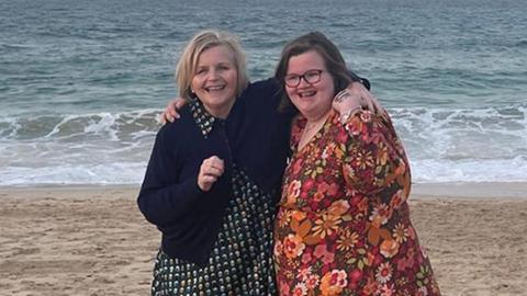 Donna Ockenden and her daughter Phoebe standing on a sandy beach with the sea behind them.