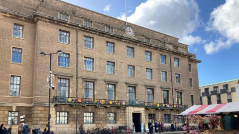 A five-storey Victorian-looking building with large windows. In front are a row of bikes and a market stall is on the bottom right hand side. 