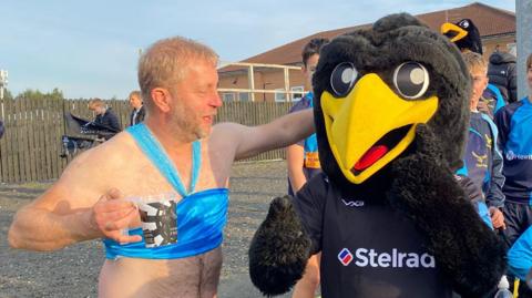 A man with a beer dressed as Princess Jasmine larking about with a person dressed as a giant black bird