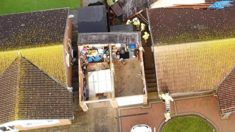 A garage is seen from above. Its roof has ripped off. 