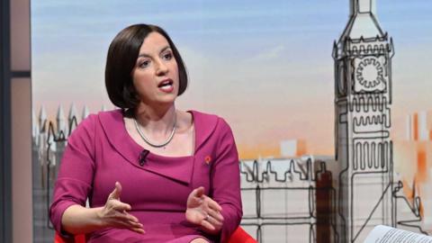 Bridget Phillipson, a woman with dark hair in a bob, wearing a fuchsia pink outfit in front of a stylised graphic of the Houses of Parliament on the set of Sunday with Laura Kuenssberg