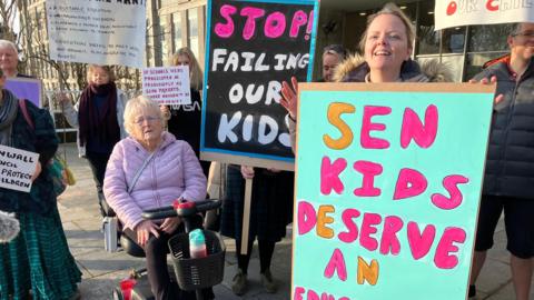 Several people seen holding colourful signs. One reads SEN KIDS DESERVE AN EDUCATION while another reads STOP FAILING OUR KIDS.  