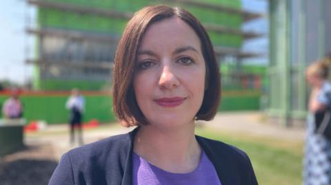 Bridget Phillipson, wearing a purple top and blue jacket, looks into the camera on a bright sunny day.