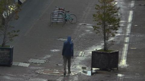 Man walks along wet Edinburgh pedestrian walkway wearing hoodie