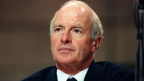 A colour photo taken earlier in his career, shows him with silver hair wearing a navy suit and tie.