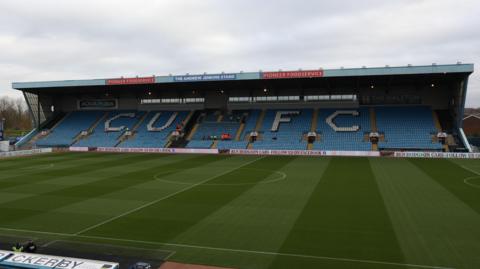 A view of Carlisle's Brunton Park East Stand with 'CUFC' written on the blue seats