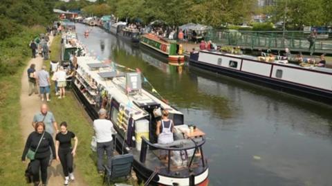 A view of canal boats, awnings and people on a canal towpath