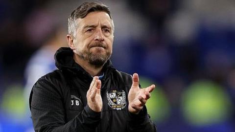 Jon Brady claps the crowd after a Port Vale match. He is wearing a black club hoodie.