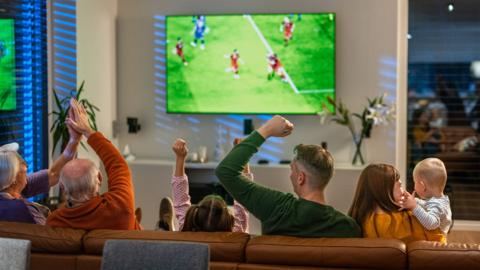Excited Multigenerational Family Watching Football Match in Cozy Living Room - stock photo