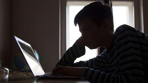 A silhouette of a boy reading the screen of a laptop