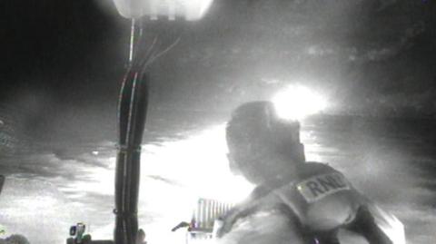 A blurry black and white photo showing an RNLI crew member and bright lights.