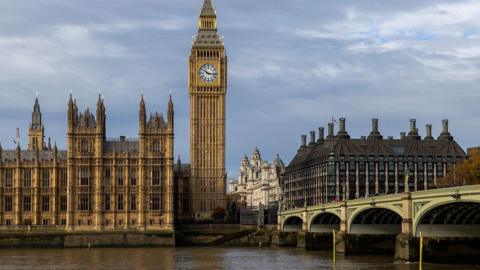 The Elizabeth Tower, known as Big Ben, and the Palace of Westminster beside the River Thames, with Westminster Bridge in the foreground under cloudy skies.