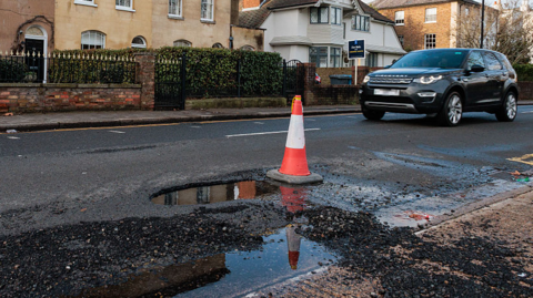 A car approaches a pothole marked with a traffic cone in Windsor on 12.1.26.