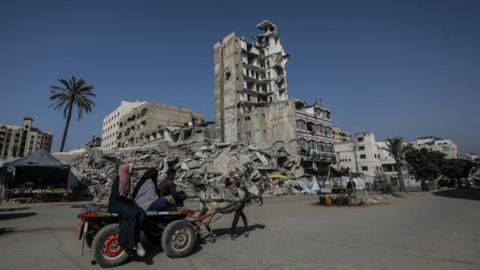 Displaced Palestinians ride on a carriage pulled by a horse on a road in Gaza City surrounded by ruined buildings 