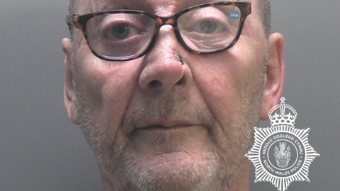James Hughes police mugshot. He has stubble and is wearing spectacles
