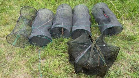 Six of the crayfish traps that have been removed from the canal are lined up side by side on a patch of grass.