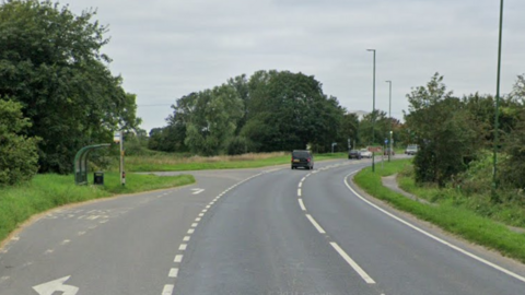 A Google Street image of a bus stop to the left of a road.