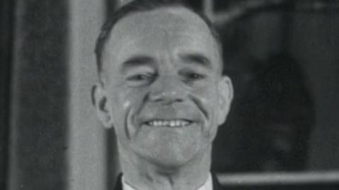 A screenshot from a black and white archive film from 1952.  Albert Gunter is smiling proudly and wearing his bus driver uniform.