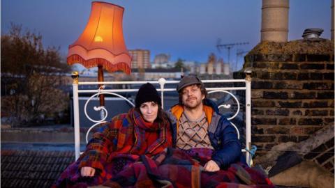 Dan Edelstyn and Hilary Powell sitting on a bed on their roof